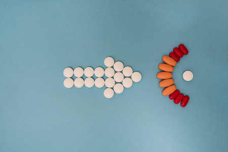 Stock photo of a bunch of different pills placed on a blue background in the shape of an arrow....