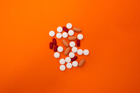 Stock photo of a bunch of different pills on an orange background. There is nobody on the picture.