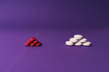 Stock photo of two piles of different pills placed on a purple background. There is nobody on the...