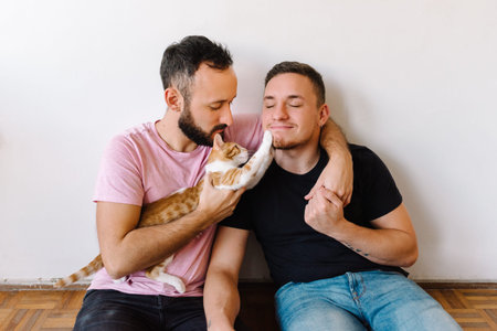 Stock photo of two caucasian homosexual men sitting down and playing with their orange and white...