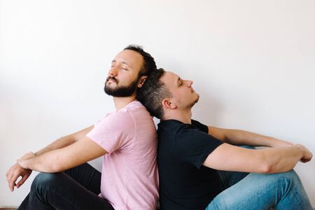 Stock photo of two caucasian homosexual men sitting back-to-back. They look calm and happy.の写真素材