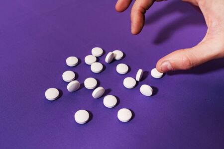 Stock photo of someones hand pinching a single tablet on a purple background. The person is unrecognizable.の写真素材