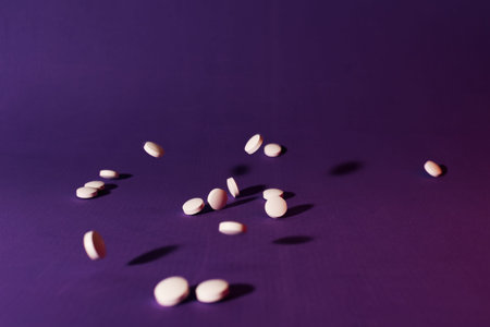 Stock photo of a bunch of pills falling down on a purple background. There is nobody on the picture.