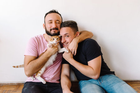 Stock photo of two caucasian homosexual men sitting down and playing with their orange and white tabby cat.の写真素材