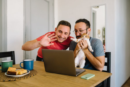 Stock photo of two caucasian adult men holding an orange and white tabby cat while laughing in front...