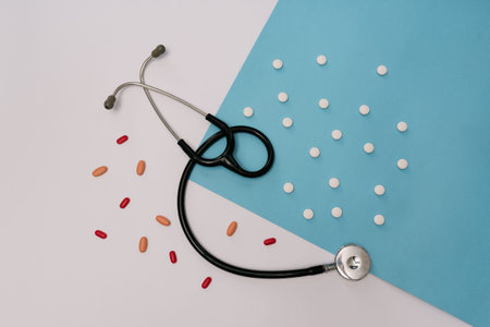 Stock photo of a stethoscope surrounded by different pills on a white and blue background. There is...