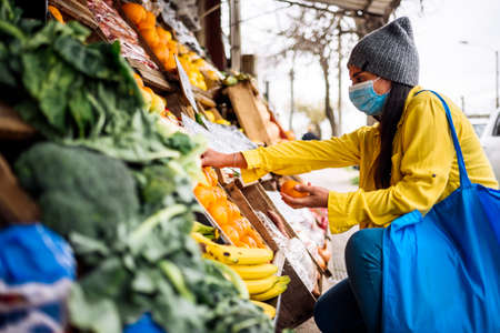 Stock photo of young woman wearing face mask buying fruit in greengrocer's shop.の写真素材