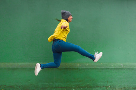 Stock photo of happy girl wearing yellow jacket jumping and having fun in the street.