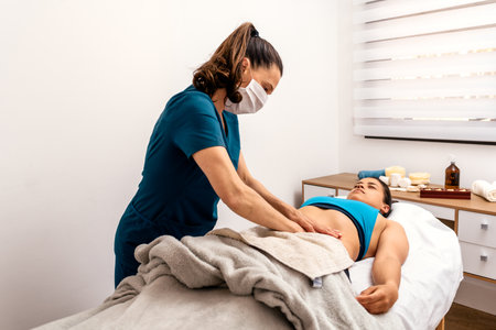 Stock photo of physiotherapist wearing face mask giving massage to patient lying in stretcher.の写真素材