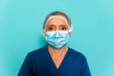 Stock photo of healthcare professional wearing face mask and disposable hair net looking at camera against blue background.の写真素材