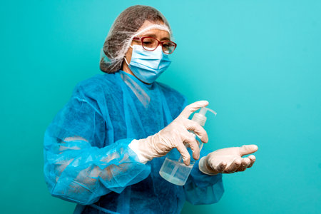 Stock photo of unrecognized healthcare worker wearing protective clothing applying hand sanitizer against blue background.の写真素材