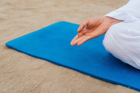 Close up of unrecognized man sitting in yoga mat in the beach doing yoga poses.の写真素材