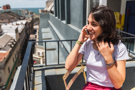Stock photo of happy woman using her mobile phone in the balcony during sunny day.