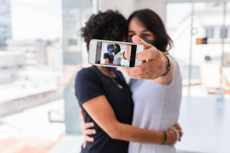 Stock photo of happy lesbian couple wearing face mask due to  taking photo at home.の写真素材