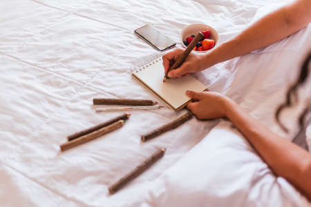 Stock photo of unrecognized girl writing notes in little notebook and eating fruit.の写真素材
