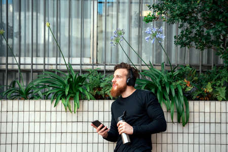Happy bearded man using his phone and listening to music after doing workout outdoors.の写真素材