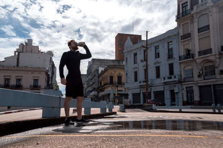 Happy bearded man in the city drinking water after doing workout outdoors.の写真素材