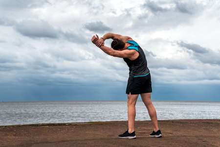 Unrecognized man wearing sports clothes in the coast stretching after working out.の写真素材