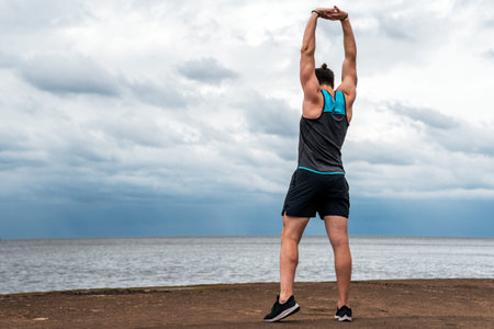 Unrecognized man wearing sports clothes in the coast stretching after working out.