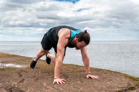 Focused bearded man doing push ups outdoors near the sea.