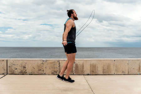 Focused bearded man using jumping rope outdoors and looking at front.の写真素材