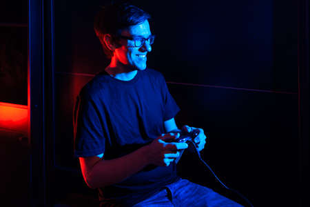 Happy adult man sitting in his room and playing video games in his computer. There are red and blue lights in the room.の写真素材