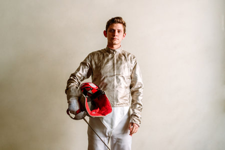 Young man wearing fencing suit and holding rapier looking at camera against white background.の写真素材