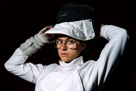 Young and expressive girl wearing fencing suit looking at camera against black background.の写真素材