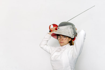 Young and expressive girl wearing fencing suit looking at camera against white background.