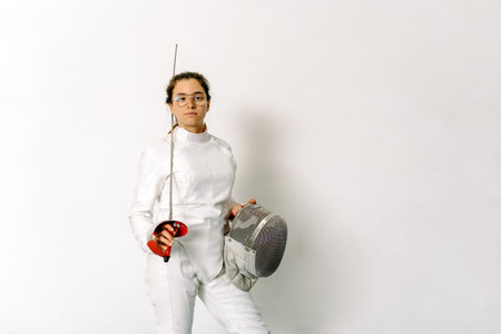Expressive girl wearing fencing suit and holding rapier looking at camera against white background.