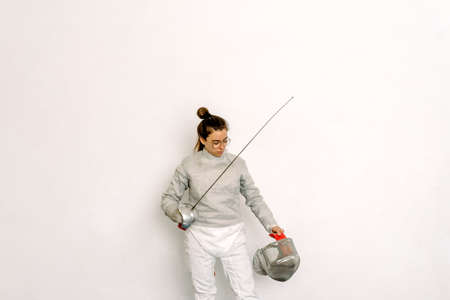 Expressive girl wearing fencing suit and holding rapier against white background.の写真素材