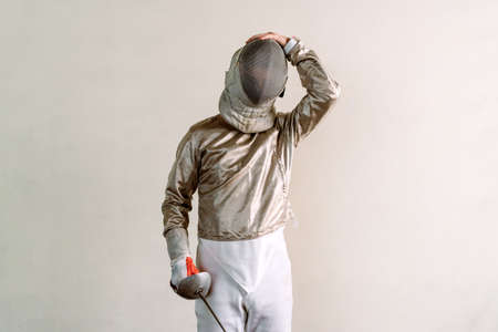 Young man wearing fencing suit and holding rapier against white background.の写真素材