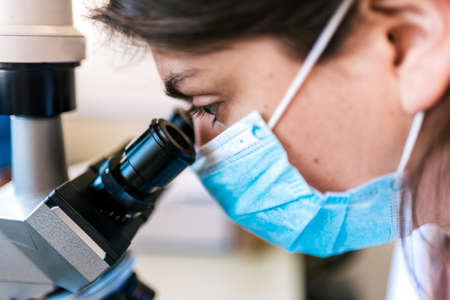 Close up of female scientist wearing face mask using a microscopy in her lab.の写真素材