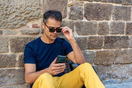 Young latin man with mobile phone sitting outsideの写真素材