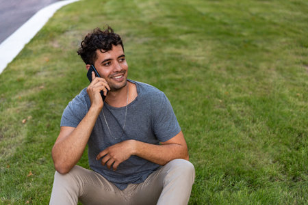 Young latin man sitting in the grass talking by mobile phone.