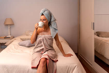 Young latin woman freshly bathed drinking coffee in her bedroomの写真素材