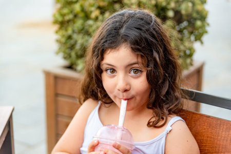 Little latin girl drinking milkshake with funny expression.
