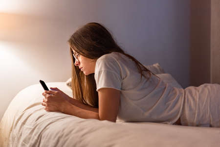Young latin woman with mobile phone lying in the bedの写真素材