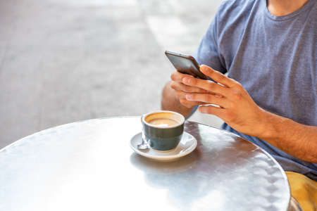 Unrecognizable young man using phone and drinking coffee.の写真素材