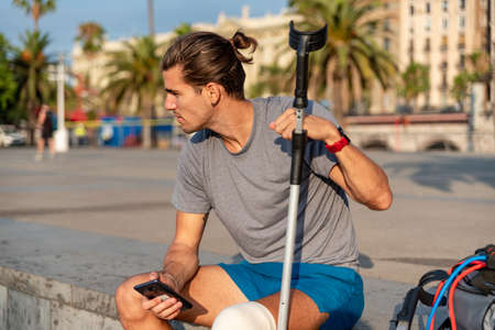 Young latin man with crutches using mobile phone after doing exerciseの写真素材