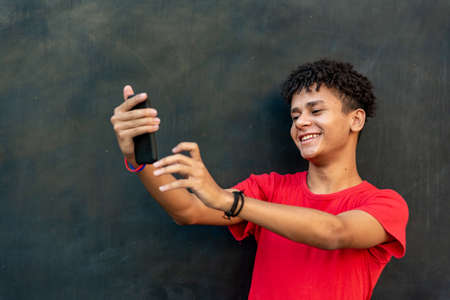 Afro latin young man taking selfie with mobile phone against a wallの写真素材