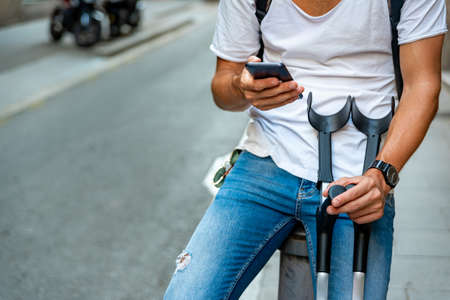 Unrecognizable young man with crutches and mobile in the streetの写真素材