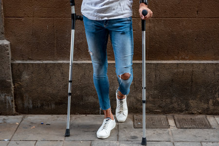 Unrecognizable young man with crutches against a wallの写真素材