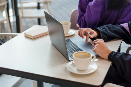 Close-up view of two people using a laptop at a coffee shop.の写真素材