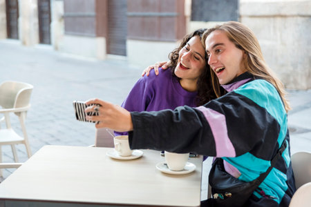 Friends taking selfies with a mobile phone while sitting at an outdoor cafe.の写真素材