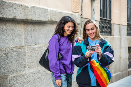 Two friends taking a selfie while walking in the street outdoors with LGBT flag.の写真素材