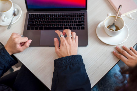 Close-up view of two people using a laptop at a coffee shop.の写真素材