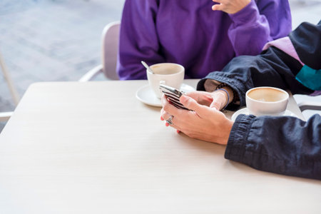 Close-up view of two people using mobile phone at a coffee shop.の写真素材