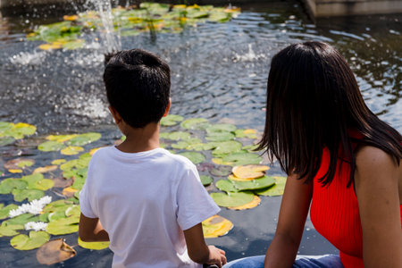 Mother and son from behind looking at the water in a park.の写真素材