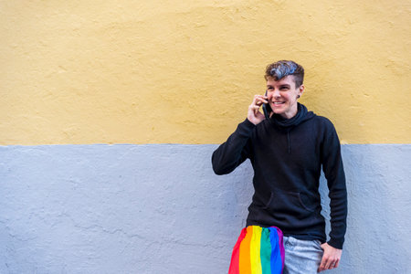 Non binary person with an lgbt rainbow flag talking on the phone outdoors.の写真素材
